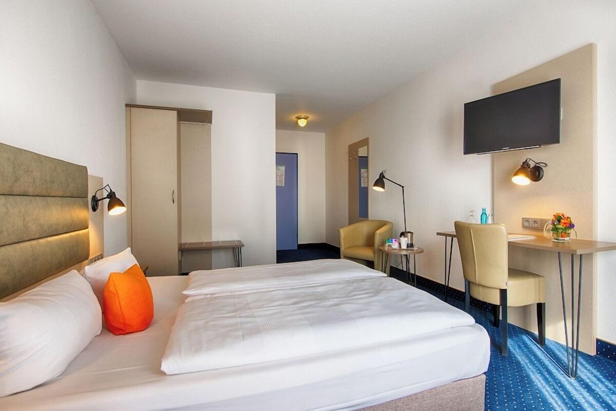 Habitación de hotel con cama, escritorio, silla, televisor montado en la pared y puerta de baño.