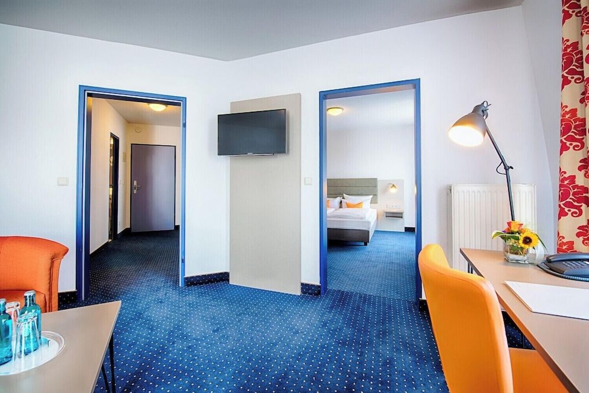 Una habitación de hotel con cama, escritorio, silla, televisor y lámpara.