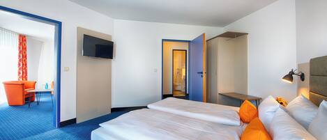 A hotel room with a large bed, a desk, a chair, and a television on the wall.