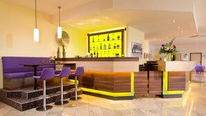 A modern bar area with a neon-lit shelf displaying bottles, a purple sofa, and matching bar stools. - ACHAT Hotel Zwickau (Zwickau)