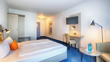 Quarto de hotel com cama, escrivaninha, cadeira, televisão e abajur.