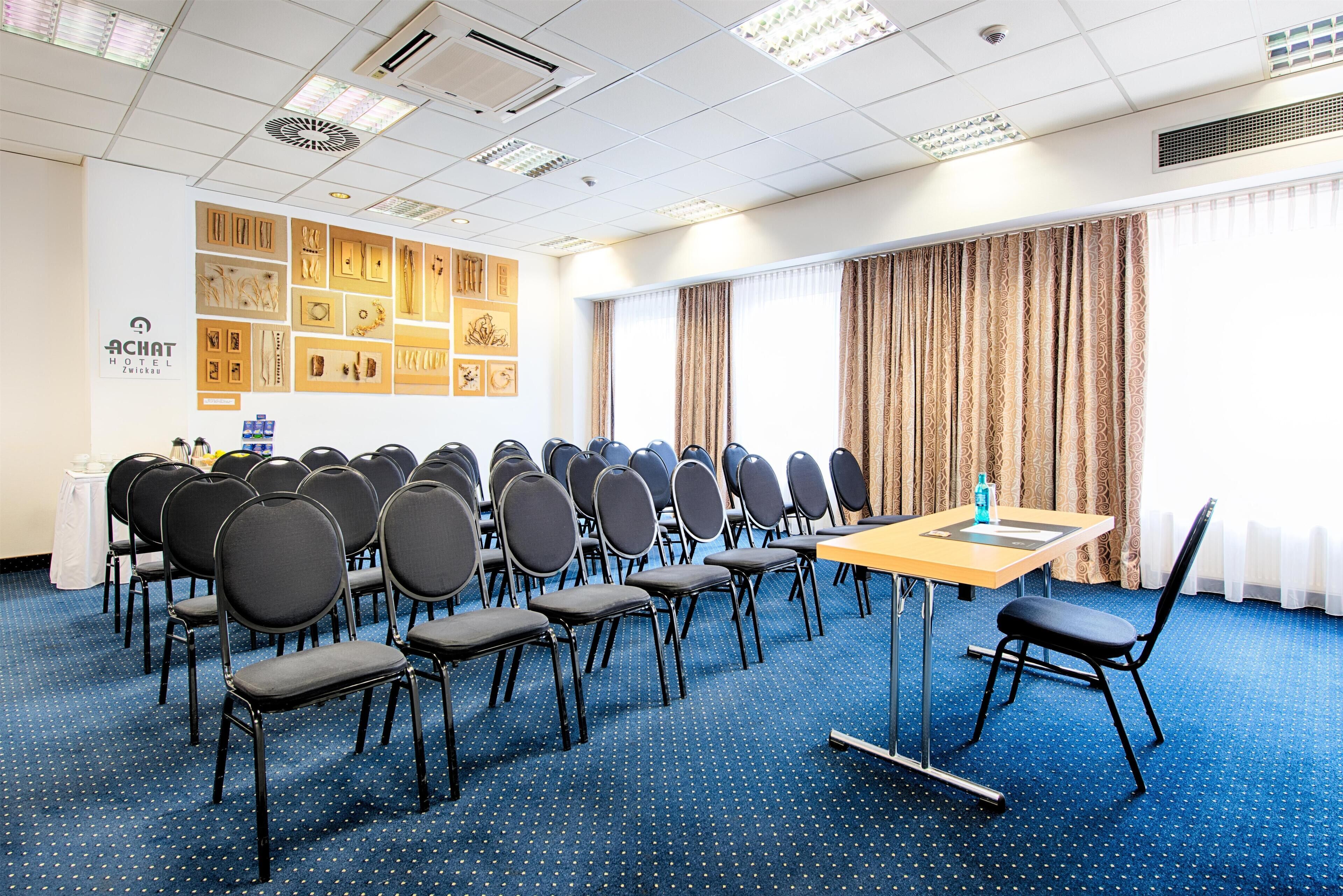 Ein Konferenzraum mit Reihen von Stühlen, einem Tisch und einer Wand mit gerahmten Bildern.