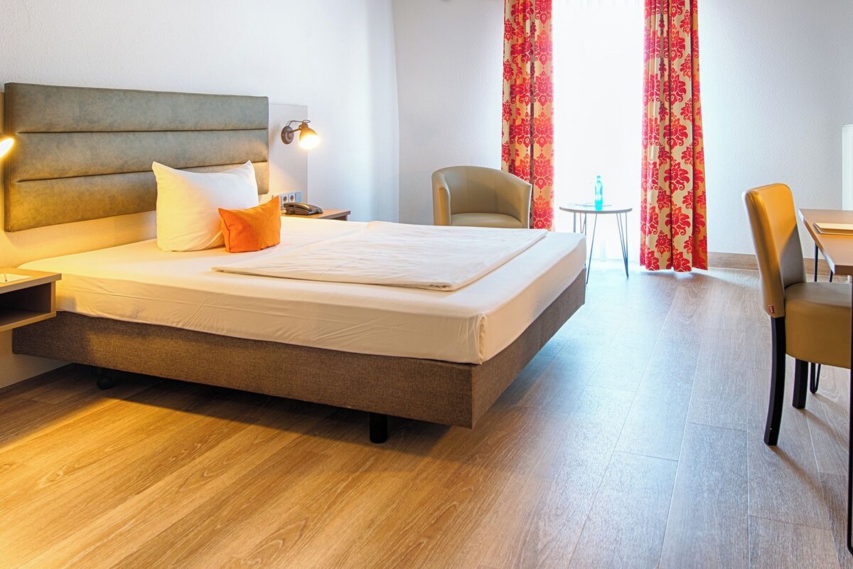 A hotel room with a bed, bedside tables, a chair, a small table, and a desk.