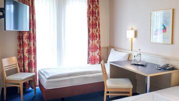 A hotel room with two beds, a desk, a chair, a TV, a lamp, and a painting on the wall.