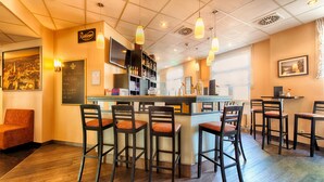 Un espace bar avec des tabourets en bois, un comptoir et un écran de télévision. On y trouve des étagères remplies de bouteilles et un tableau noir servant de menu.