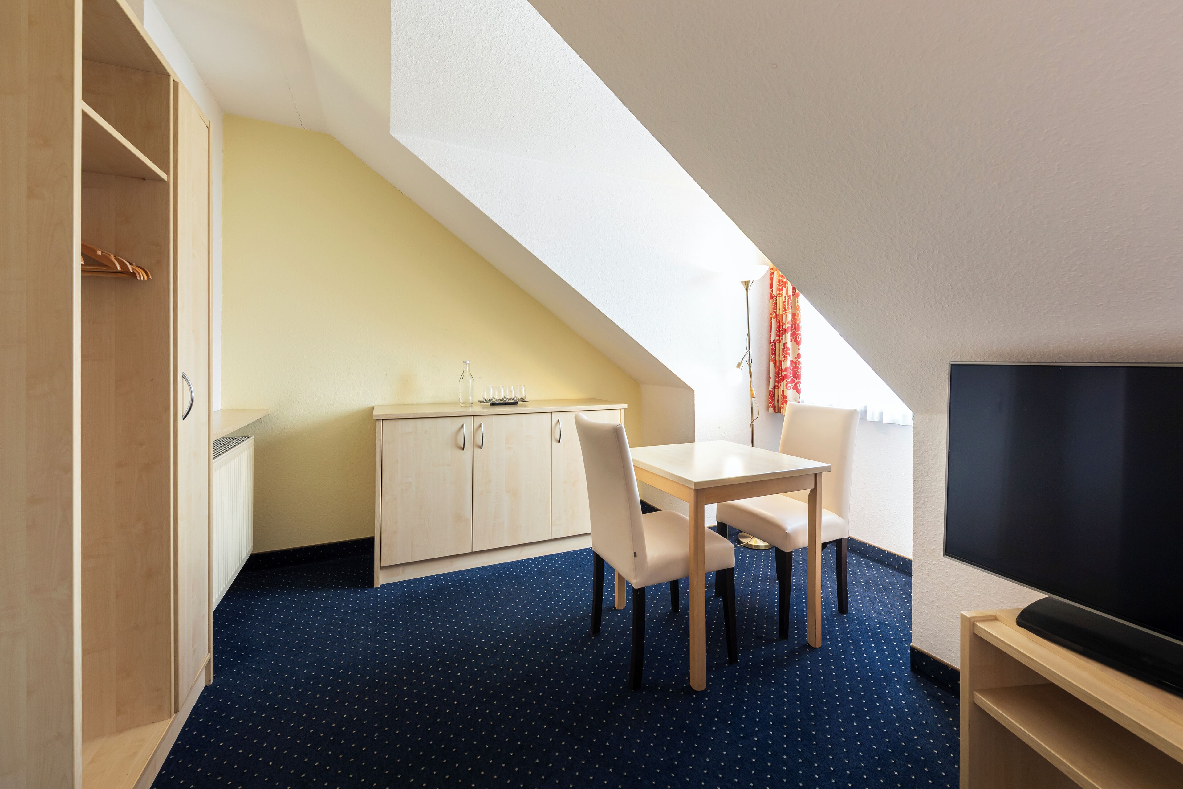 A room with a dining table, chairs, a TV, a wardrobe, and a radiator.