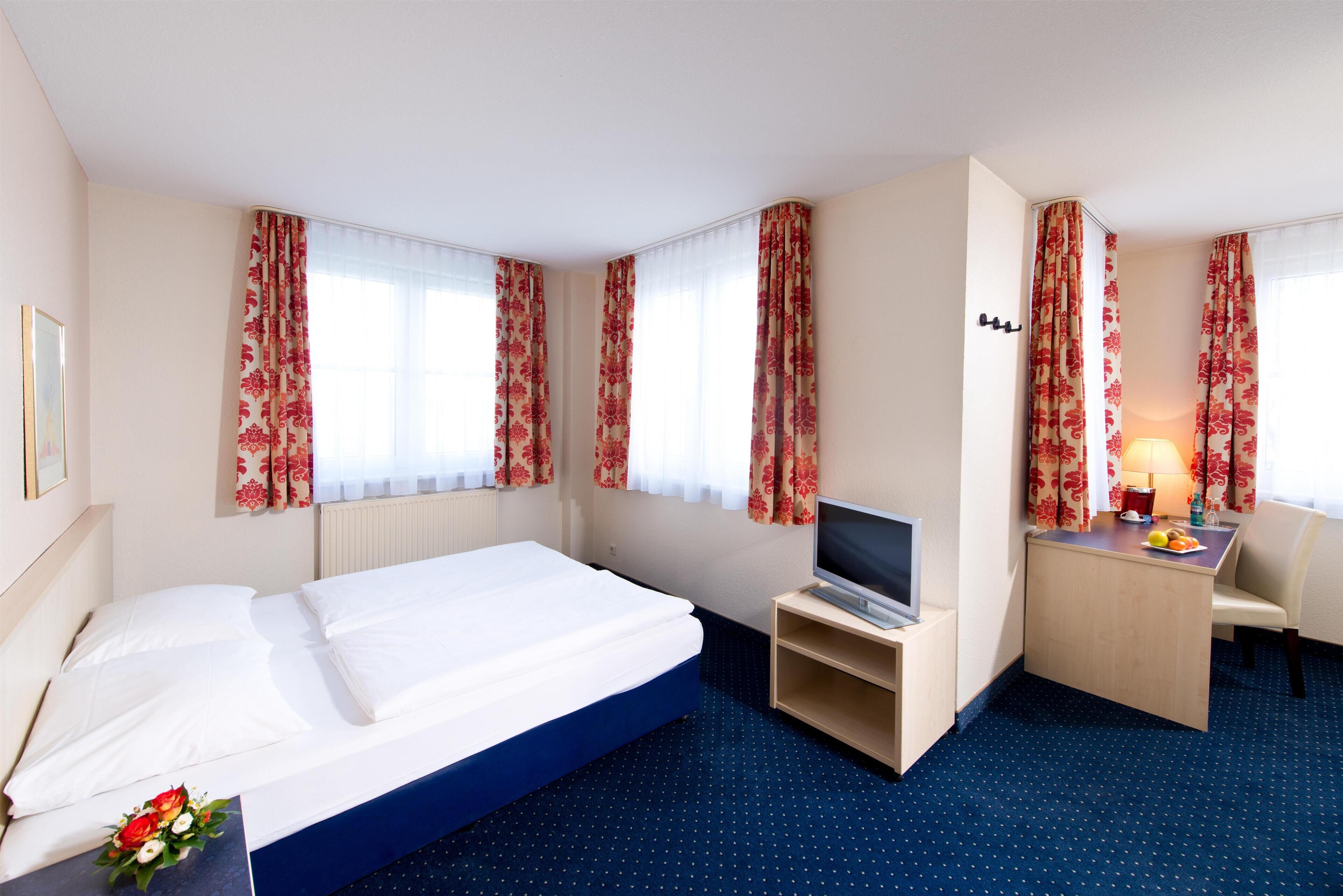 Quarto de hotel com uma cama, uma mesa com televisão e uma cadeira.