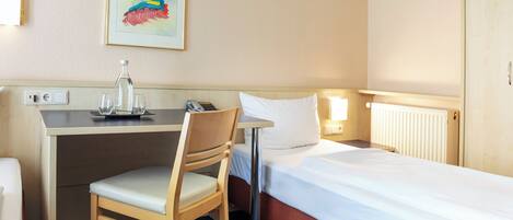 A hotel room with a bed, a desk, a chair, a lamp, a painting, and a radiator.