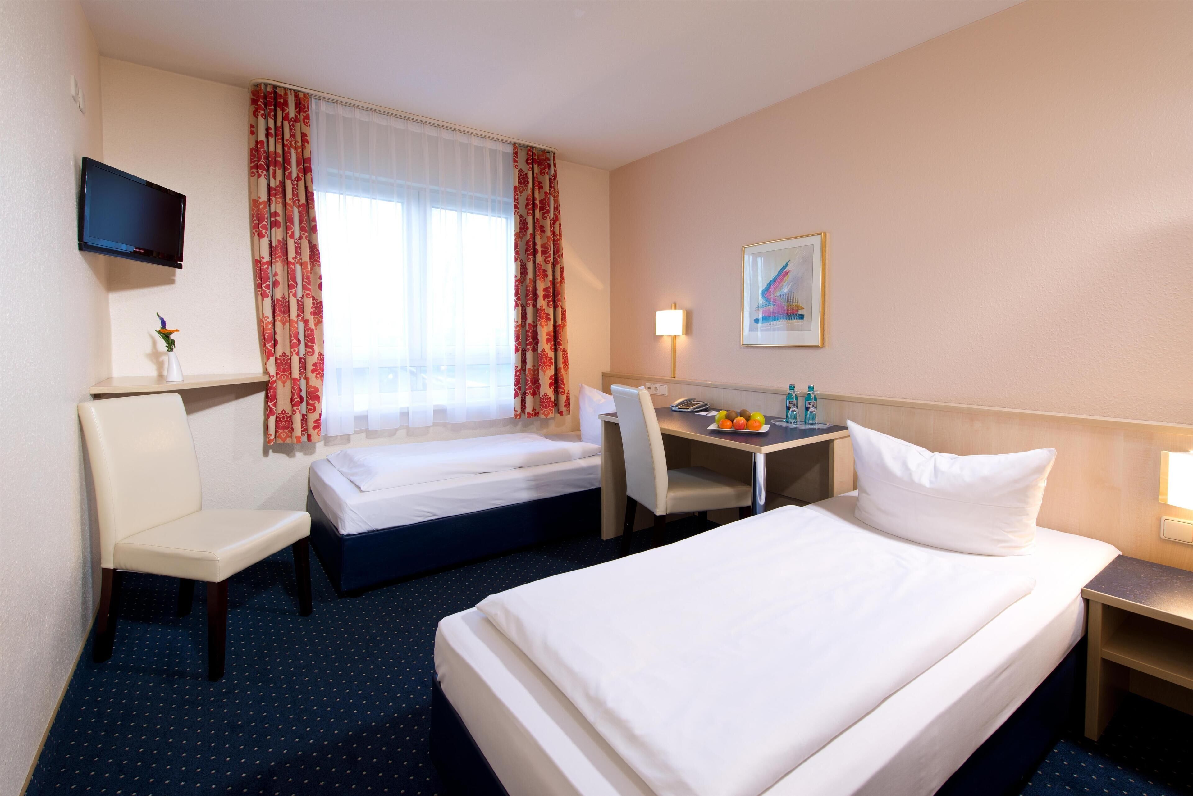 Une chambre d’hôtel avec deux lits, un bureau, une chaise, une télévision et un tableau au mur.
