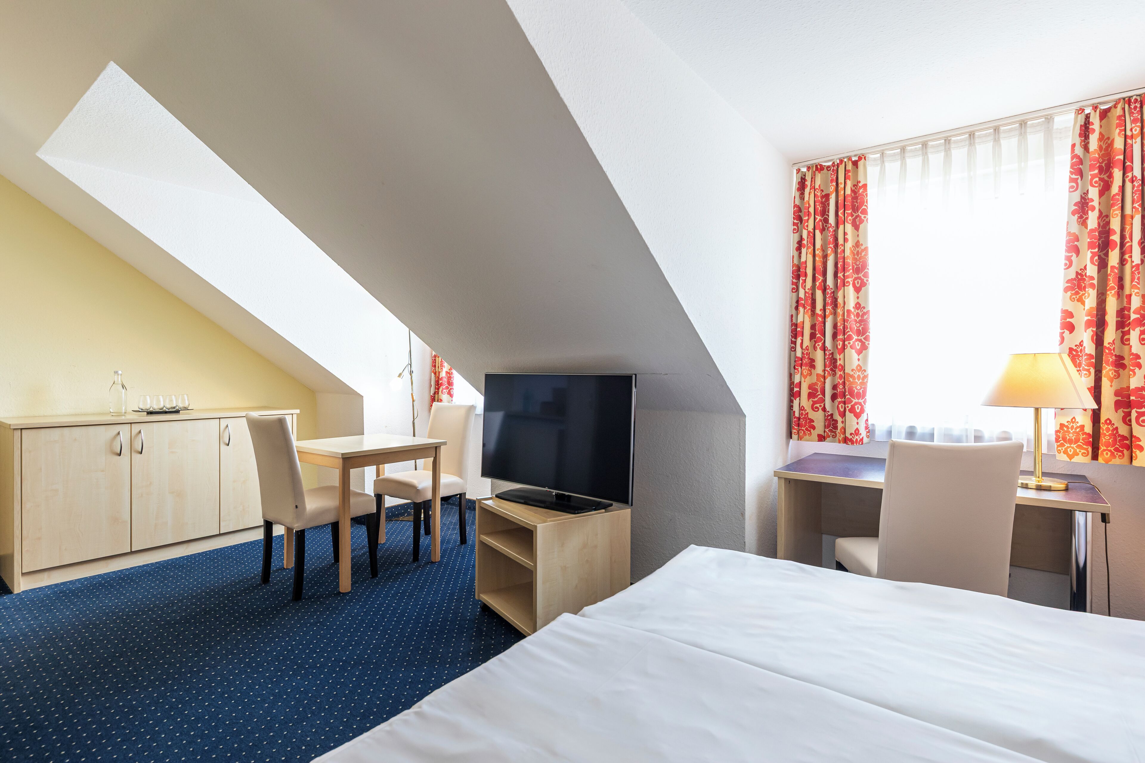 Een hotelkamer met een bed, een bureau met stoel, een televisie en een raam met gordijnen.