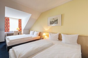 Habitación de hotel con dos camas, un escritorio, una silla y una lámpara.