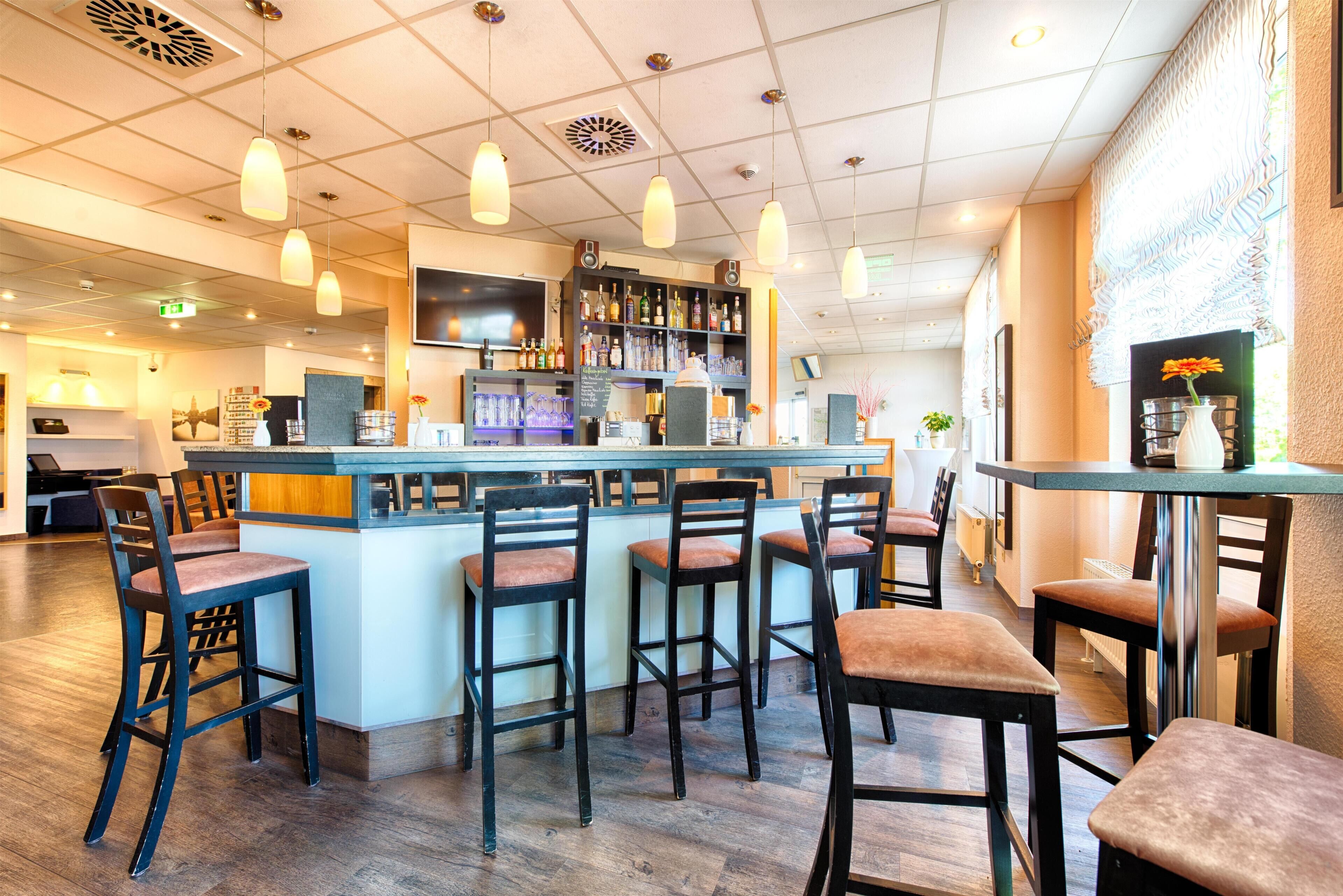 Una zona de bar con taburetes de madera, mostrador y lámparas colgantes.