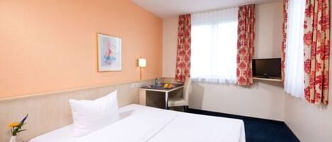 A hotel room with a bed, a desk, a chair, a TV, and a window with curtains.