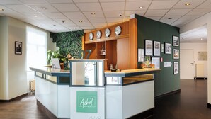 Un comptoir d’accueil avec une enseigne verte, un lambris en bois et des horloges au mur.