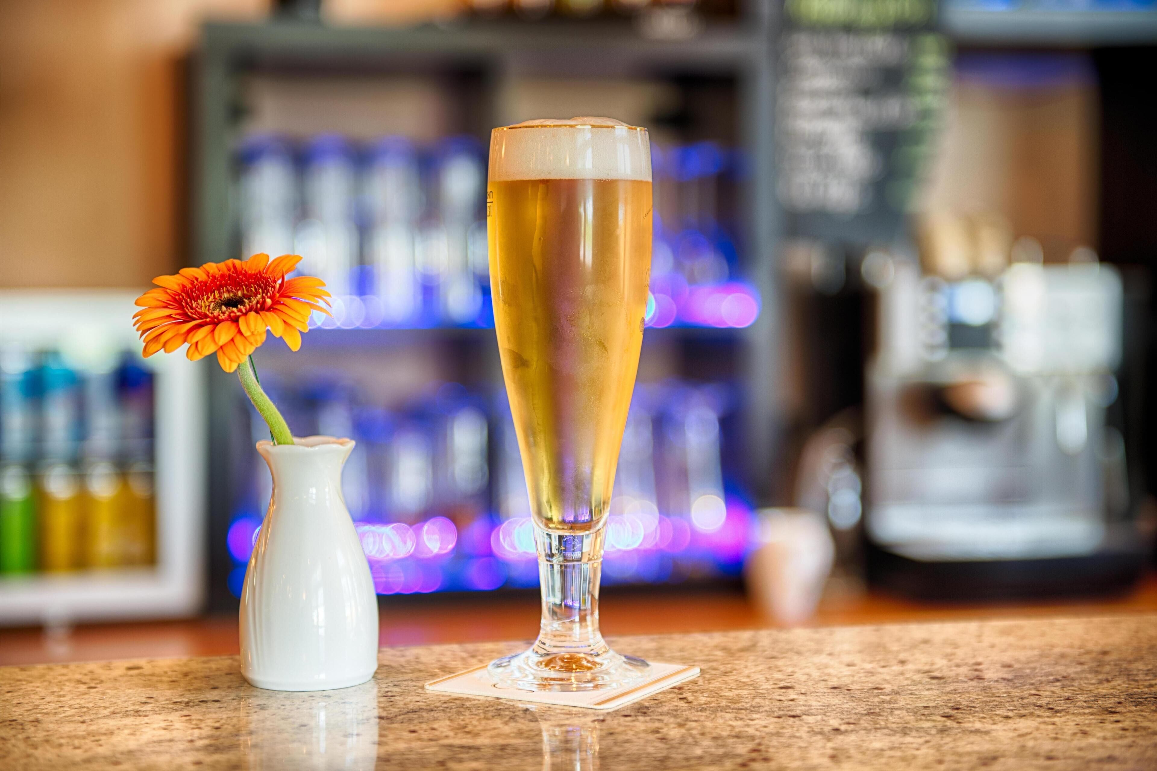 A glass of beer with a flower on the counter.