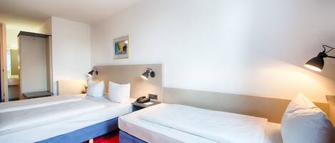Habitación de hotel con dos camas, una alfombra roja con lunares, un cuadro en la pared y una lámpara a la derecha.