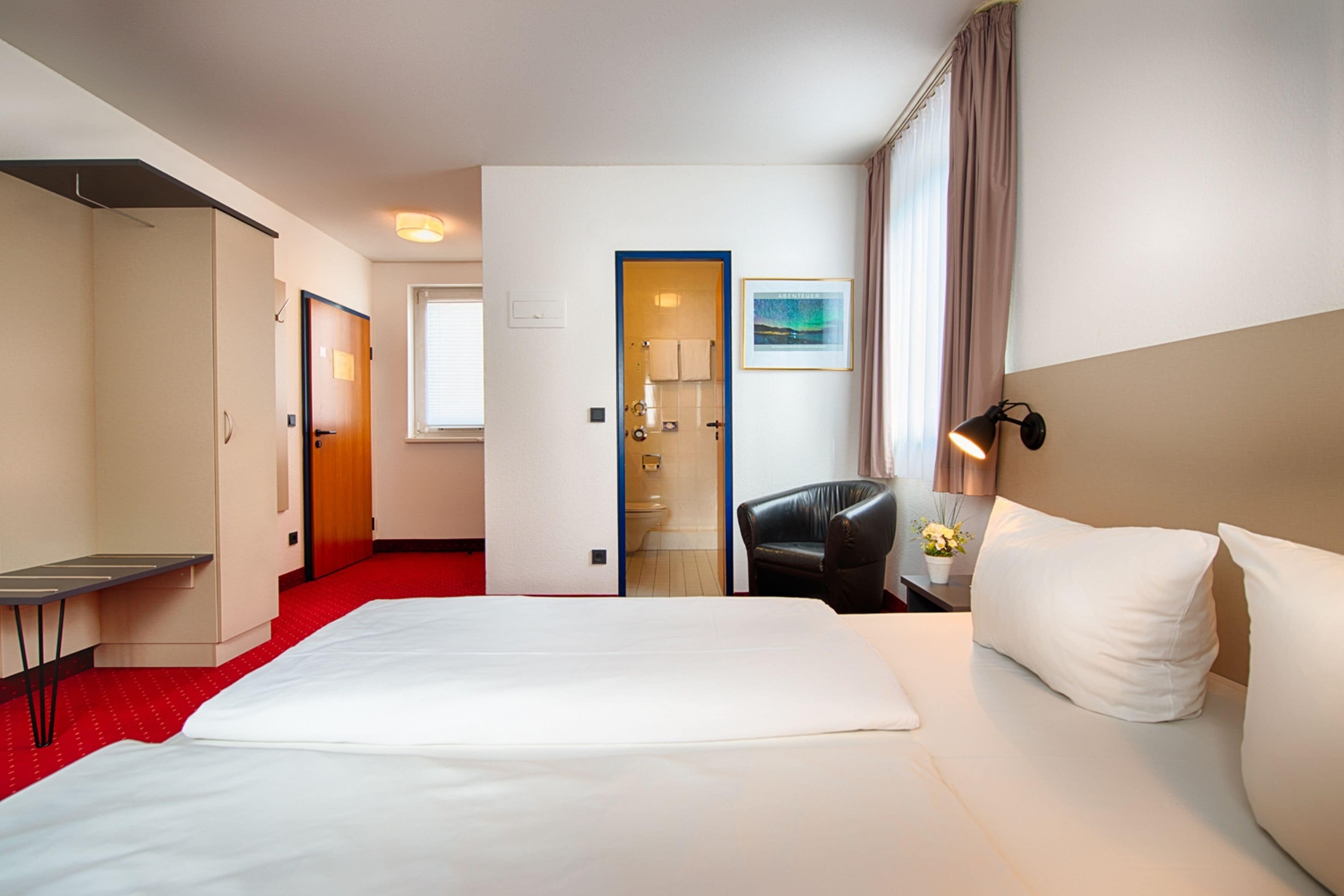 Ein Hotelzimmer mit einem großen Bett, einem Schreibtisch, einem Stuhl und einem durch eine offene Tür einsehbaren Badezimmer.