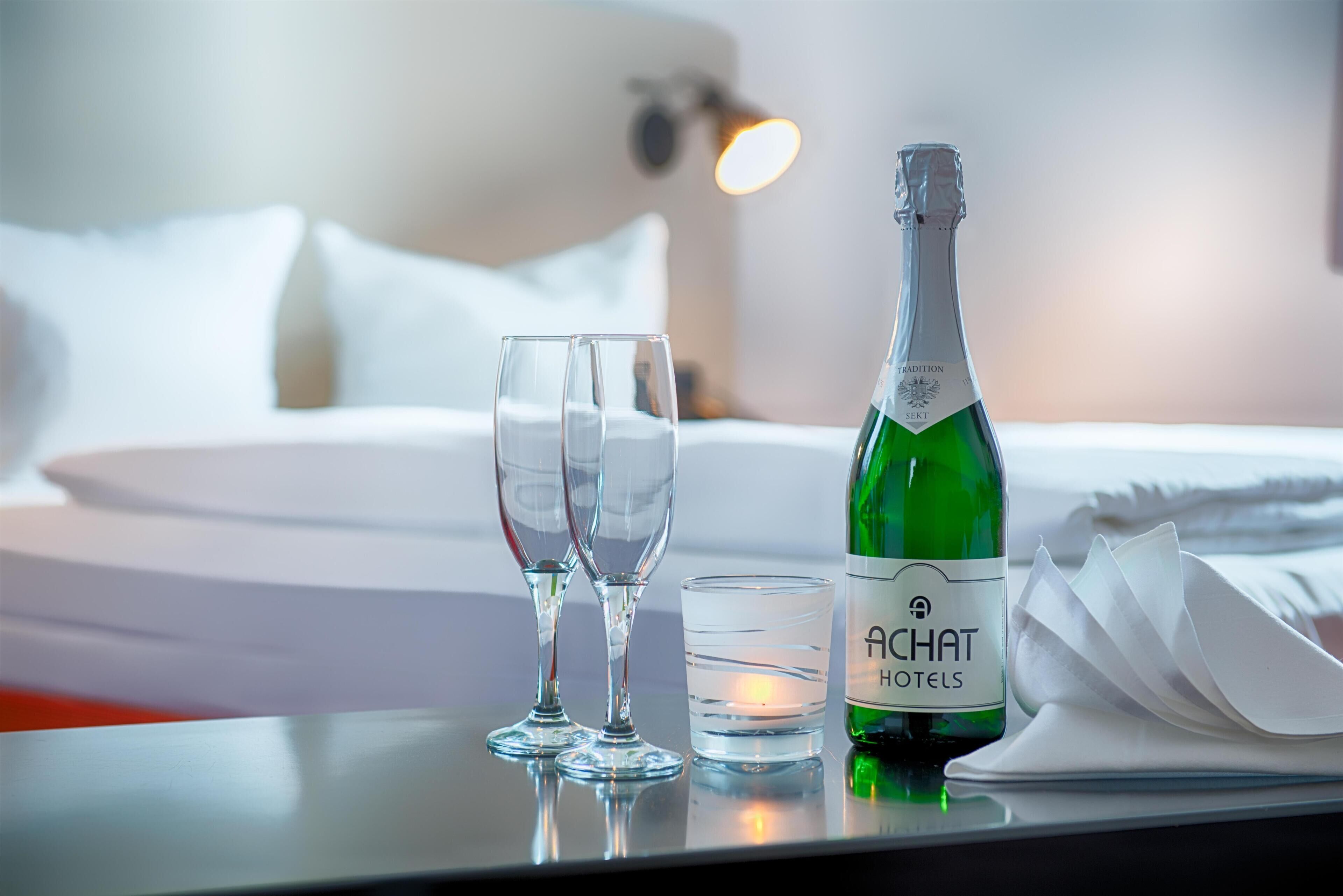 A hotel room with a bed, two wine glasses, a candle, and a bottle of champagne.