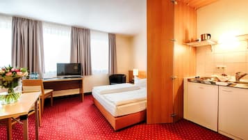 Ein Hotelzimmer mit Bett, Schreibtisch, Stuhl, Fernseher und Küchenzeile.