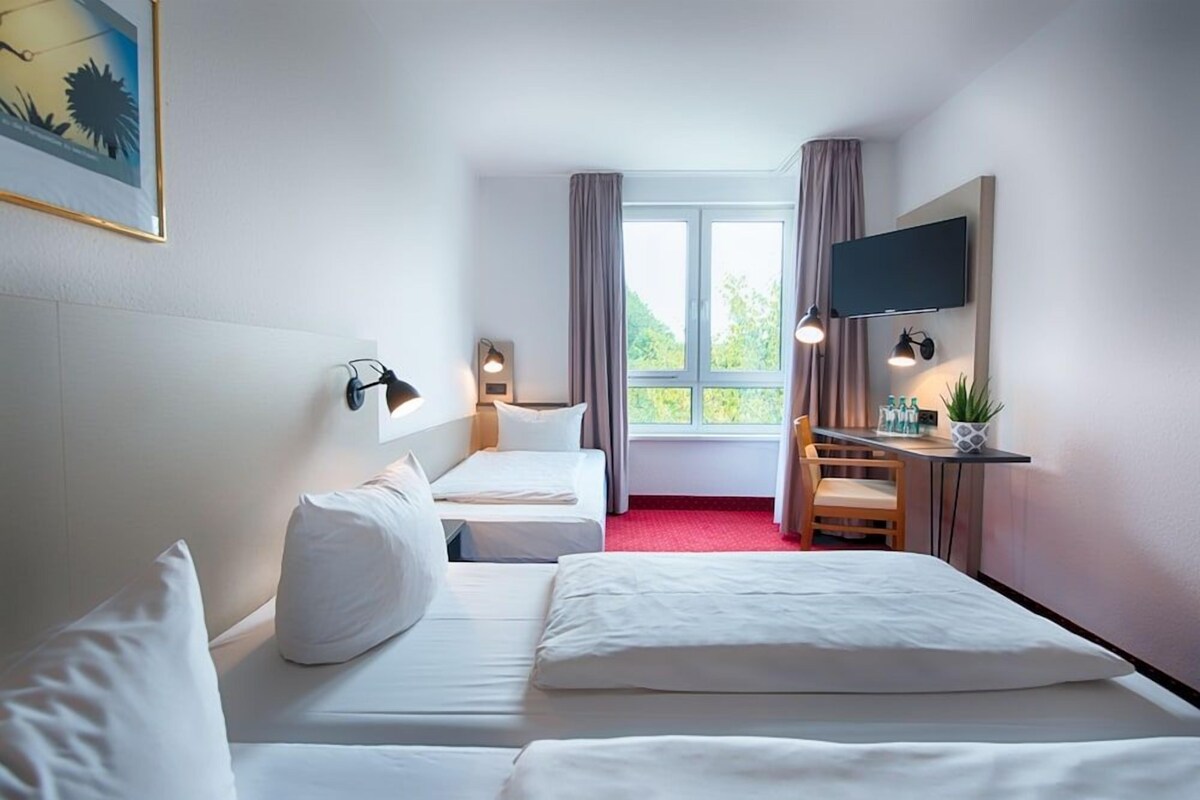 A hotel room with two beds, a desk with a chair, a TV mounted on the wall, and a window with curtains.