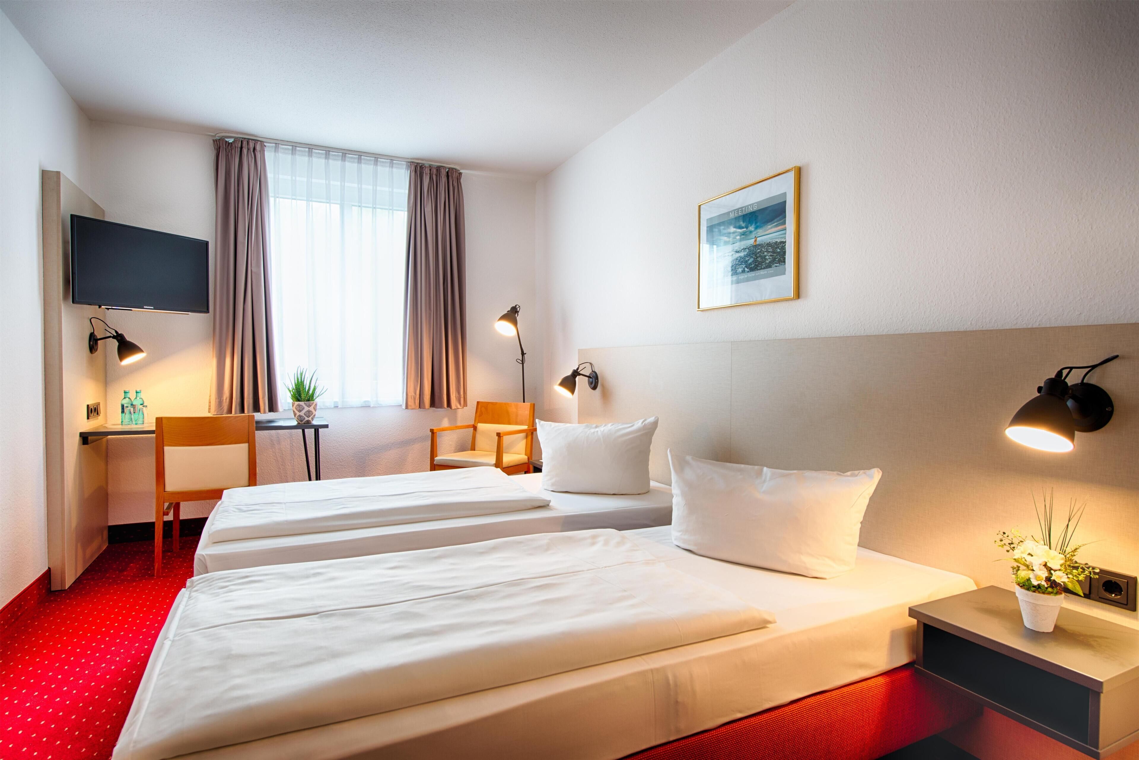 A hotel room with two beds, a desk, a chair, a TV, and a window with curtains.