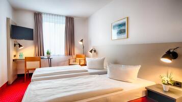 Habitación de hotel con dos camas, un escritorio, una silla, un televisor y una ventana con cortinas.