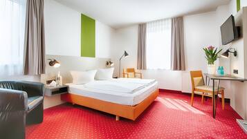 Habitación de hotel con cama, escritorio, silla, televisor y ventana con cortinas.