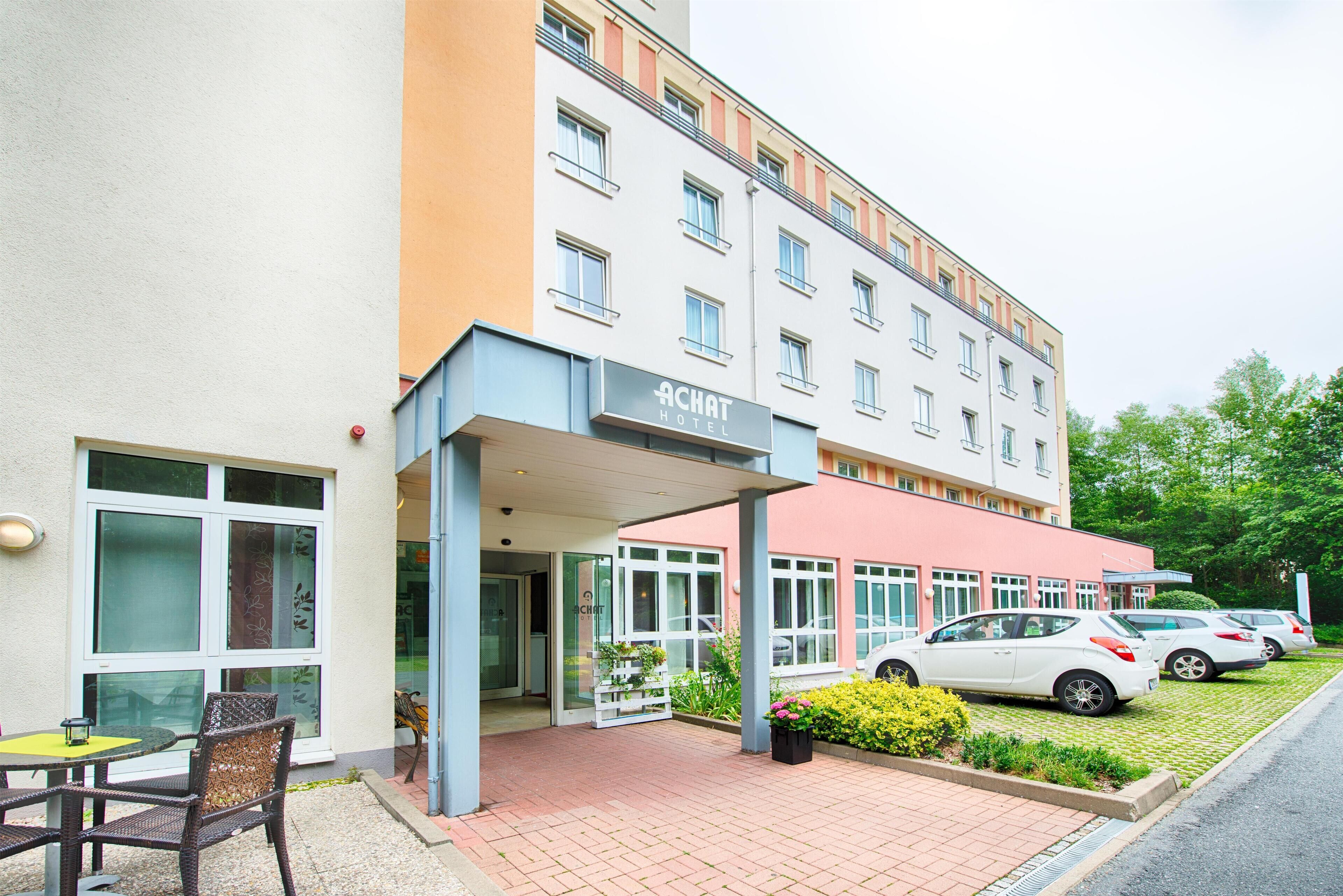A hotel entrance with a covered patio, outdoor seating, and a parking area.