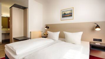A hotel room with a large bed, a nightstand, a wall-mounted lamp, and a framed picture on the wall.