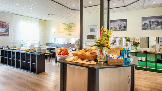 A breakfast buffet with various food items, a vase with flowers, and a sign on the wall. - ACHAT Hotel Chemnitz (Chemnitz)