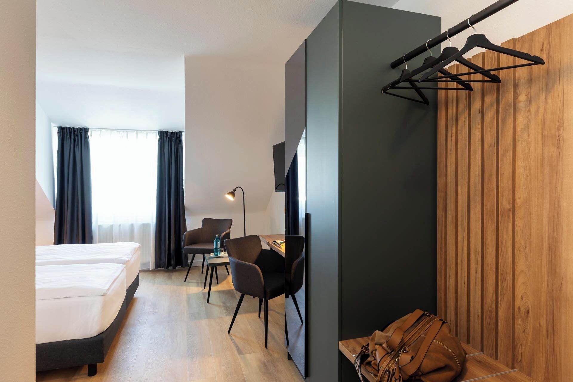 Habitació d'hotel moderna amb un llit, un escriptori, dues cadires, un televisor i una paret de panells de fusta.