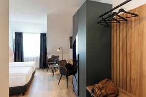 A modern hotel room with a bed, a desk, two chairs, a TV, and a wooden panel wall. - ACHAT Hotel Schwetzingen Heidelberg (Schwetzingen)