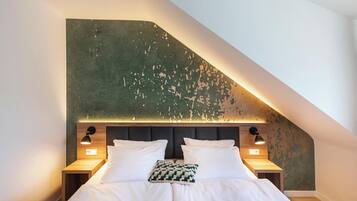 A bedroom with a sloped ceiling, a bed with white bedding, two bedside lamps, and a textured wall.