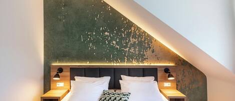 A bedroom with a sloped ceiling, a bed with white bedding, two bedside lamps, and a textured wall.