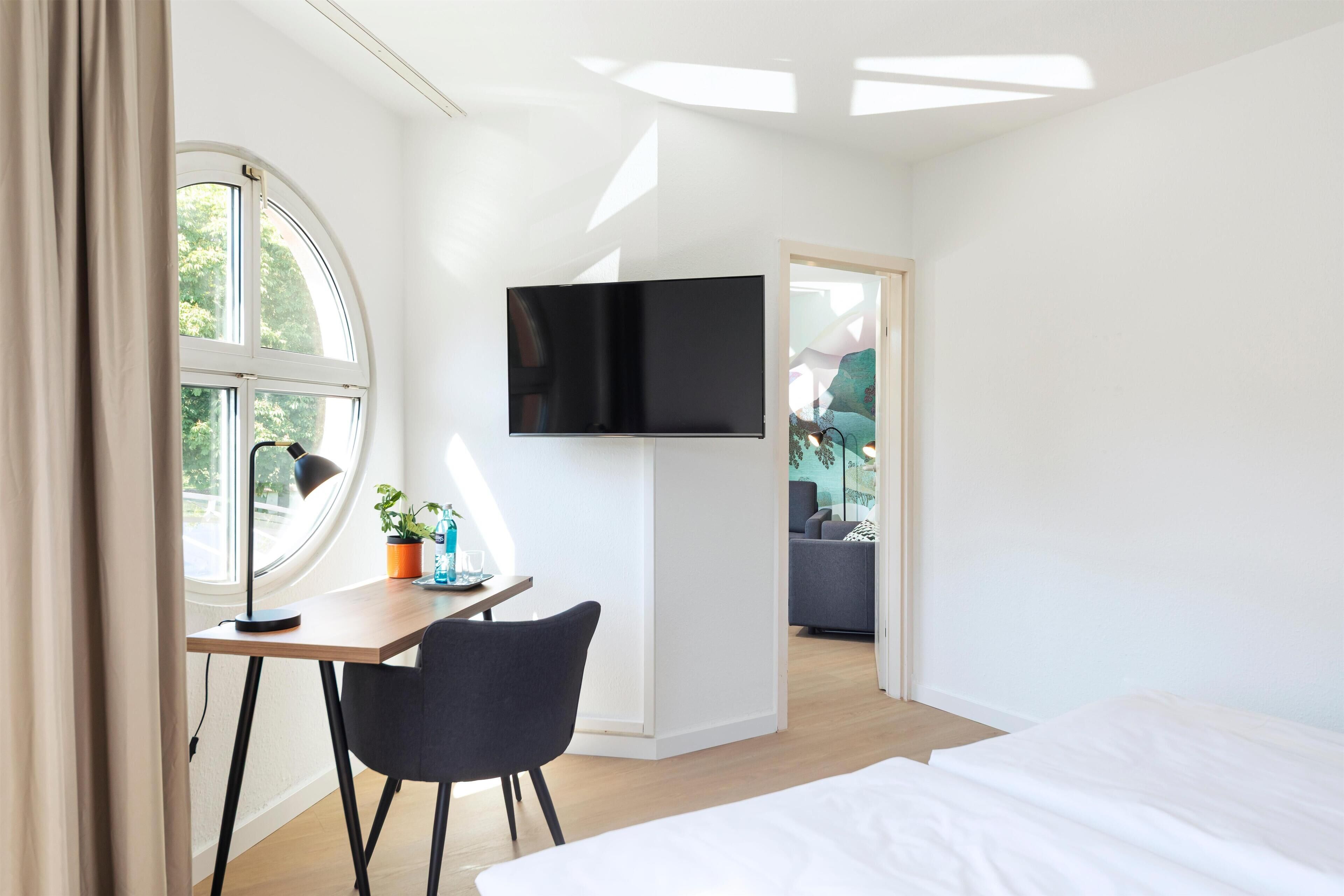 Une chambre d’hôtel moderne équipée d’un lit, d’un bureau avec une chaise, d’un téléviseur fixé au mur et d’une fenêtre avec des rideaux.