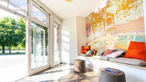 A modern lobby with a large glass door, a seating area with cushions, and a large wall mural.