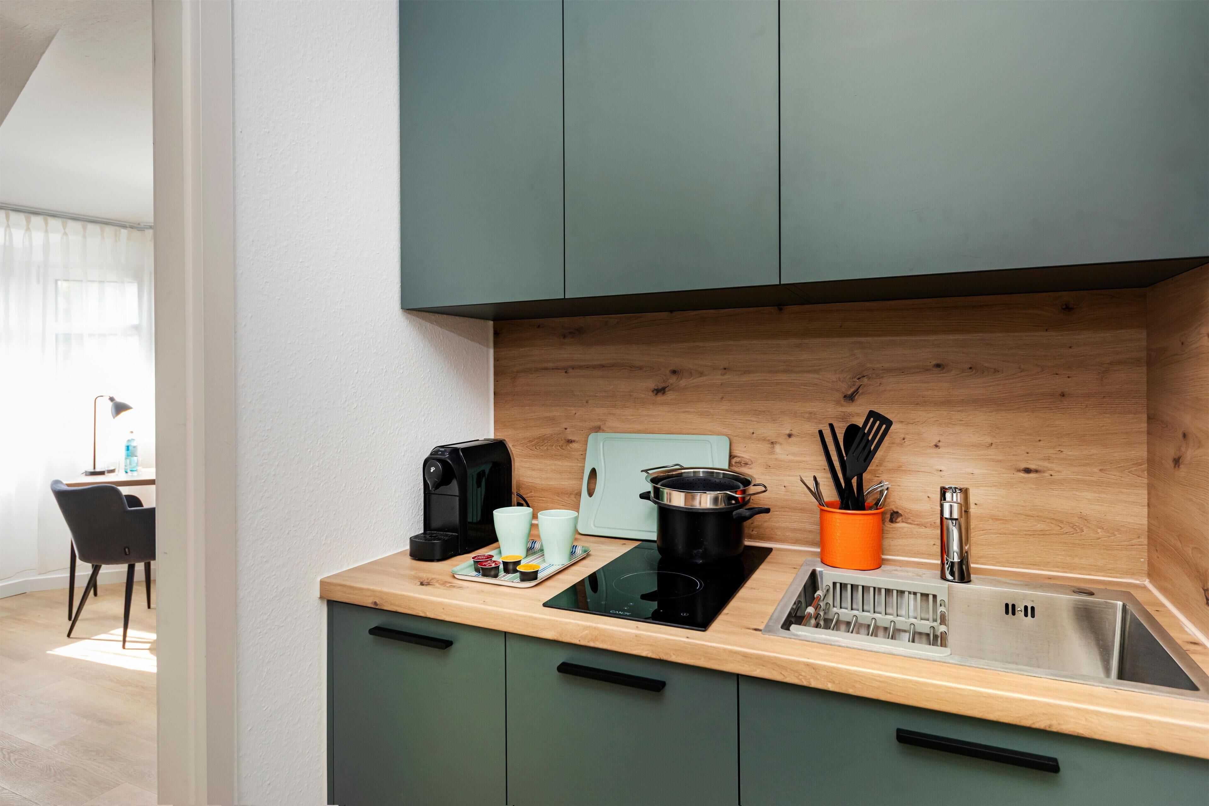 Una cocina moderna con encimera de madera, un fregadero y una estufa. Se observan armarios, una cafetera y una tabla de cortar.