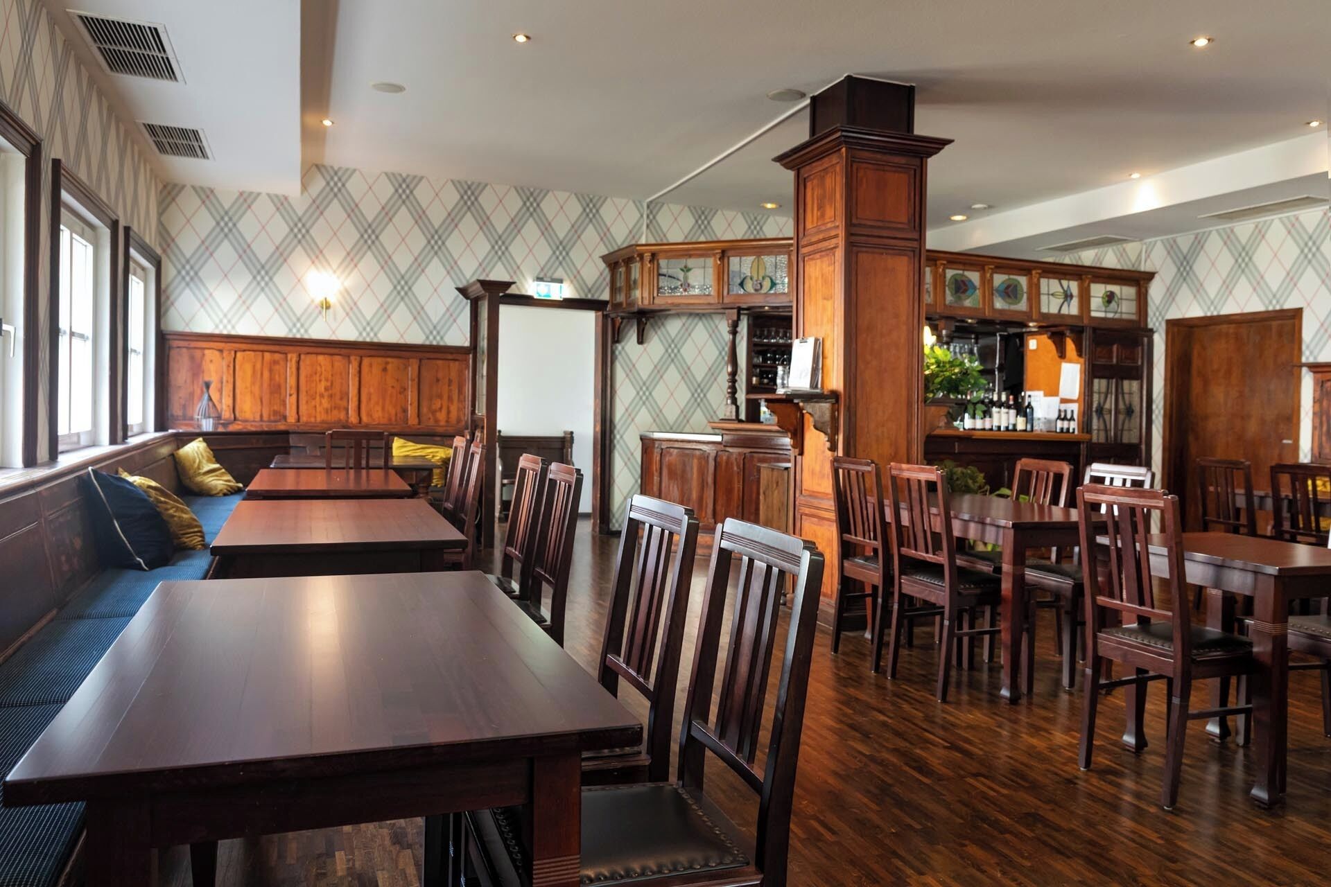 Un restaurante con mesas y sillas de madera, una zona de bar y una pared con diseño.