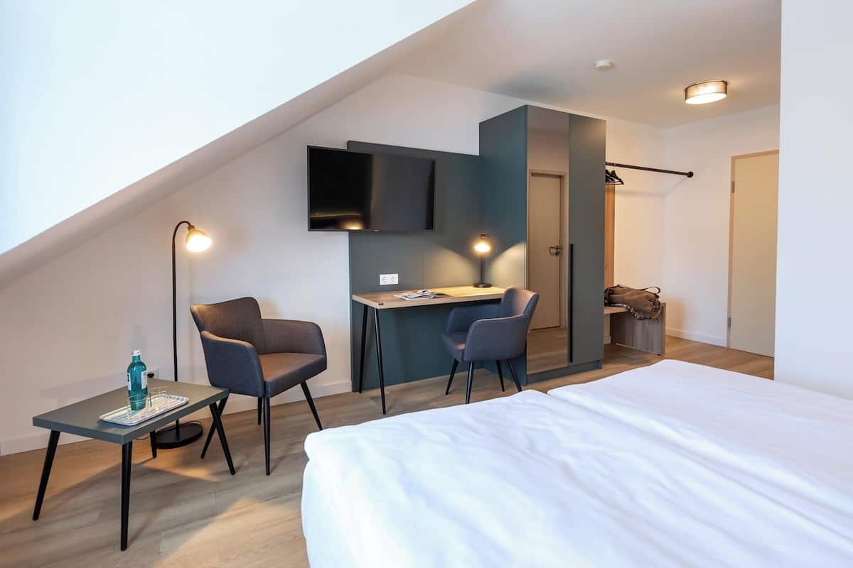 A modern bedroom with a bed, two chairs, a desk, and a TV.