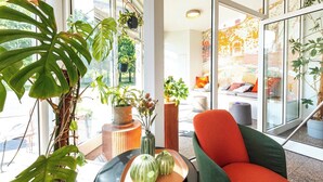 A modern living room with a large window, a red and green armchair, and various potted plants.
