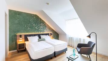 A modern hotel room with a sloped ceiling, two beds, a desk, a chair, and a large window.