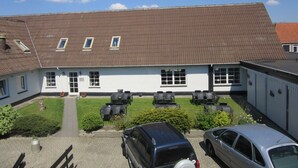 Un bâtiment blanc avec un toit brun, une allée pavée et deux voitures garées devant.