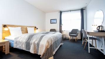 Habitación de hotel con cama, escritorio, dos sillas, espejo y ventana con cortinas.