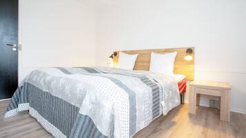 Una cama bien tendida con un edredón estampado, una mesita de noche con una lámpara y un cabecero de madera.