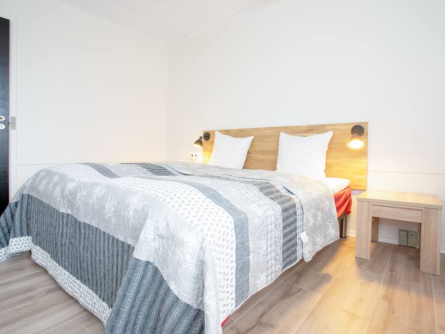 Una cama bien tendida con un edredón estampado, una mesita de noche con una lámpara y un cabecero de madera.