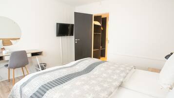 A bedroom with a bed, a desk, a chair, a TV, and a wardrobe.