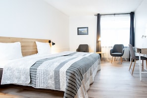 A hotel room with a bed, two chairs, a desk, and a window with curtains.