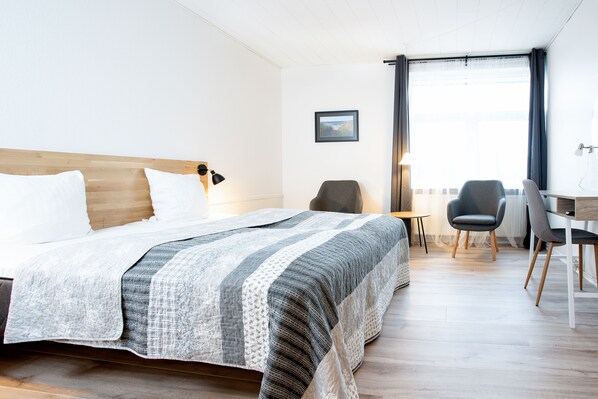 A hotel room with a bed, two chairs, a desk, and a window with curtains.