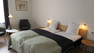 A hotel room with a bed, two bedside tables, a chair, a small table with a vase of flowers, and a wall-mounted lamp.