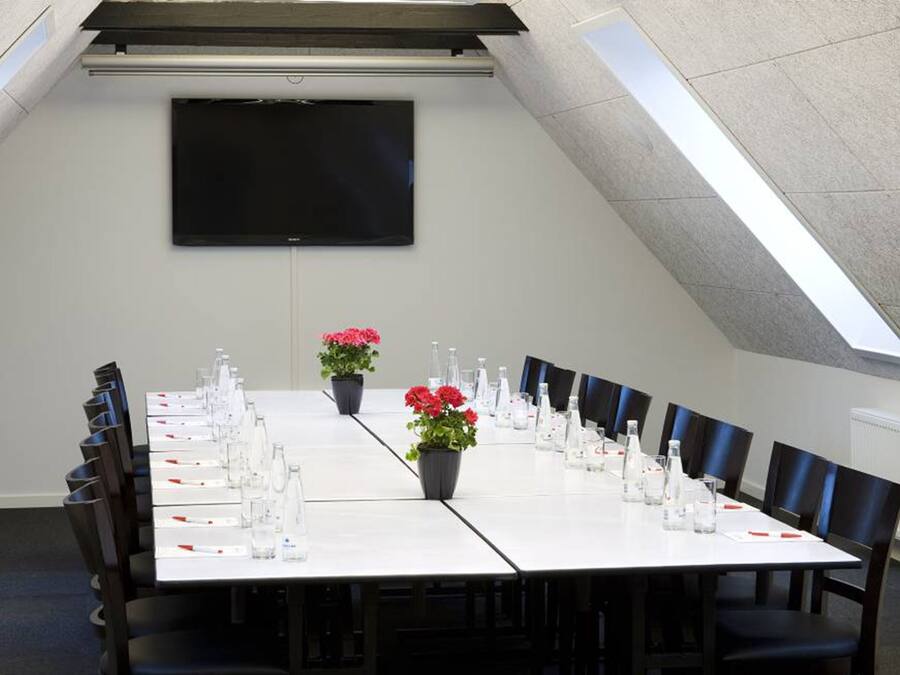 Ein Konferenzraum mit langem Tisch, Stühlen, einem Flachbildfernseher und Topfpflanzen.